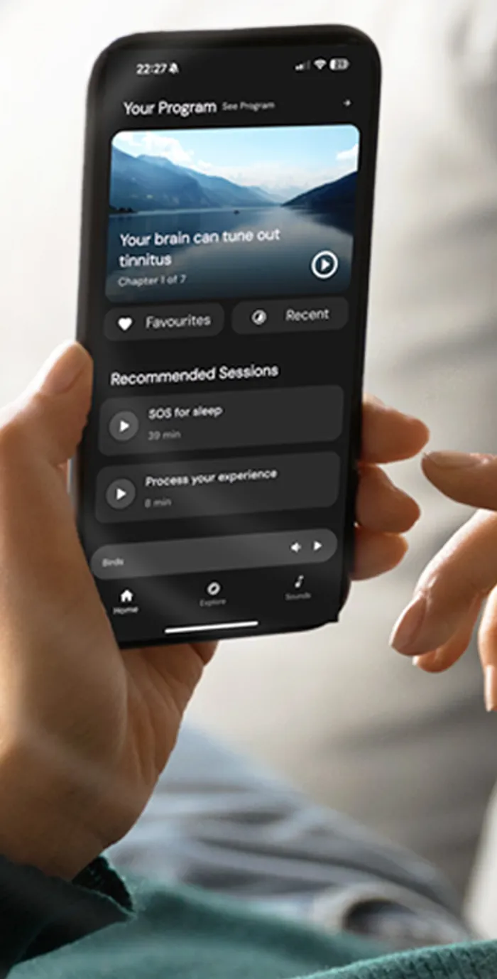 A patient holding a phone showing the Oto tinnitus program home screen, with recommended sound therapy sessions