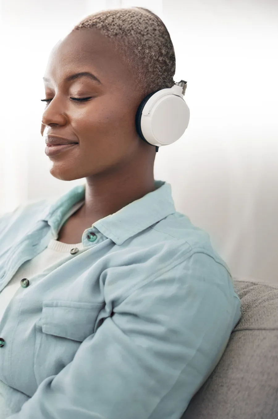A woman relaxing with headphones and her eyes closed, listening to calming sound therapy at home