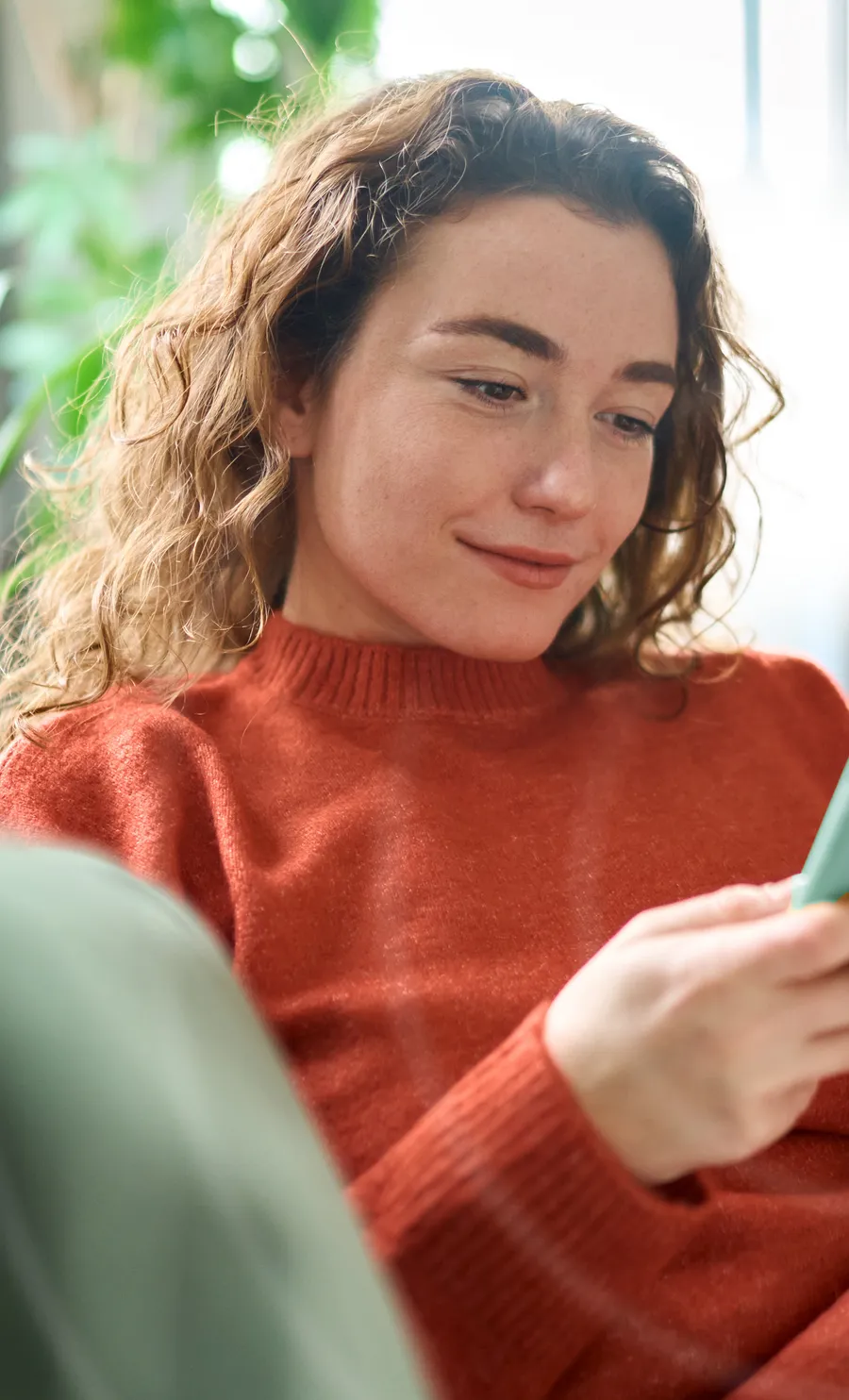 A smiling woman relaxing on her couch at home while using the Oto program on her phone